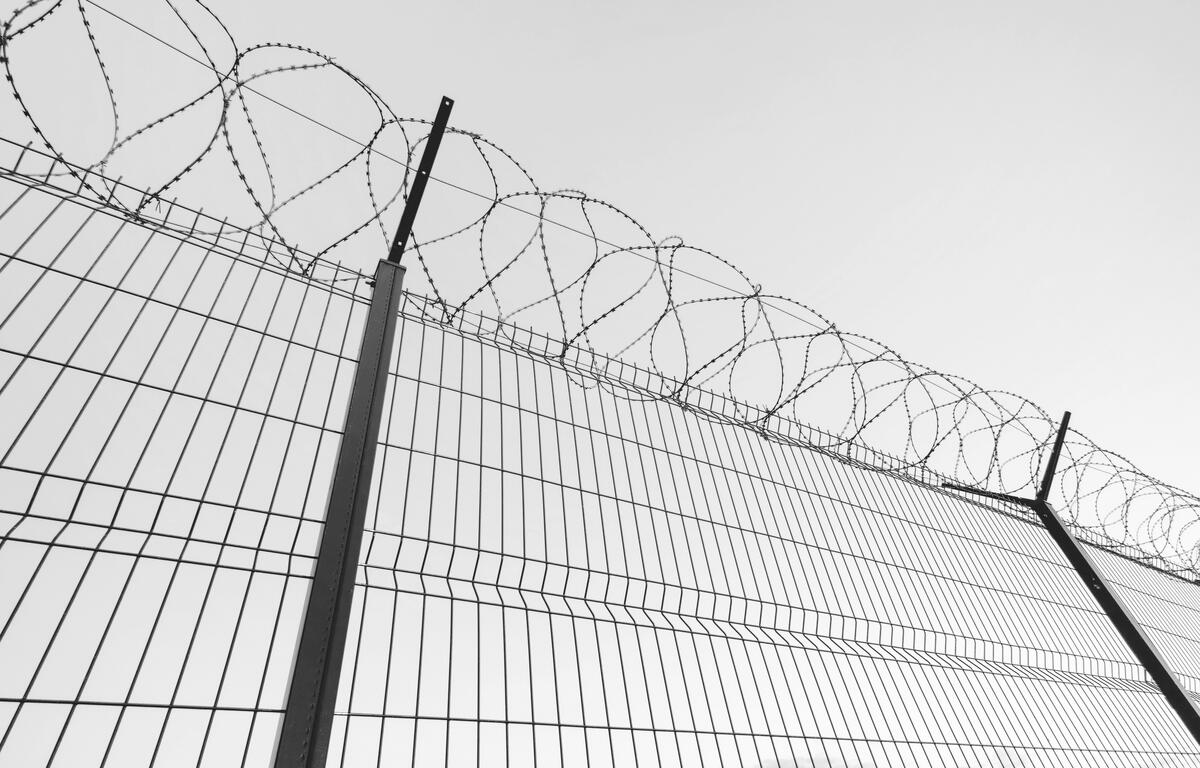 Slatted fence with barbed wire on top. Sky background behind Imprisonment concept.