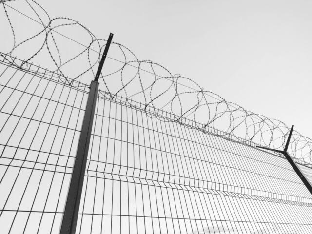 Slatted fence with barbed wire on top. Sky background behind Imprisonment concept.