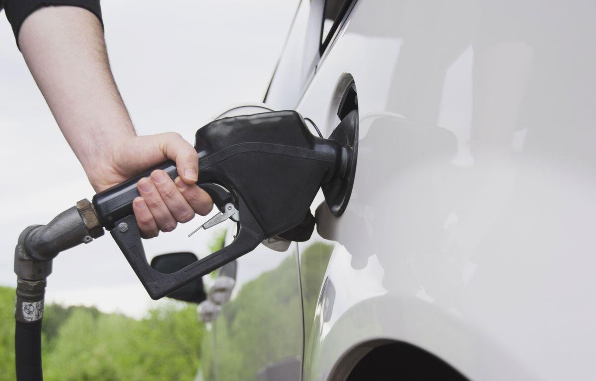 Close-up of a person pumping gas into a white car using a black fuel nozzle.