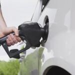 Close-up of a person pumping gas into a white car using a black fuel nozzle.