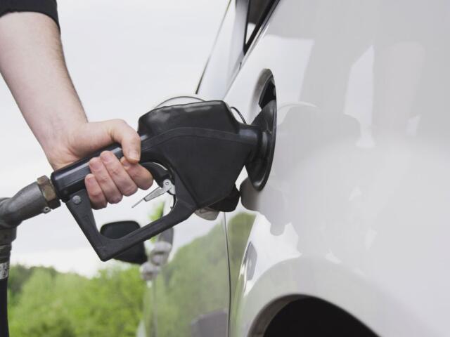 Close-up of a person pumping gas into a white car using a black fuel nozzle.