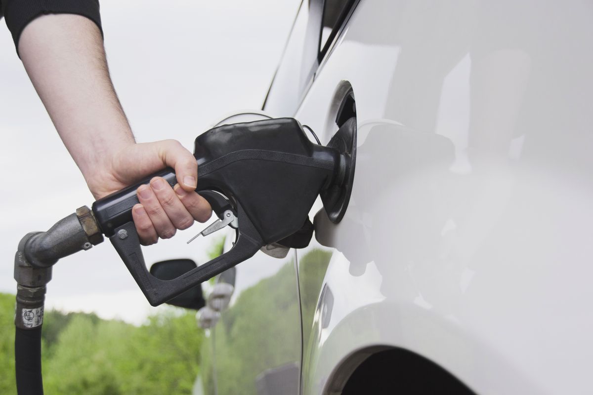 Close-up of a person pumping gas into a white car using a black fuel nozzle.