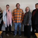 Five adults posing and smiling in a classroom in front of a whiteboard.