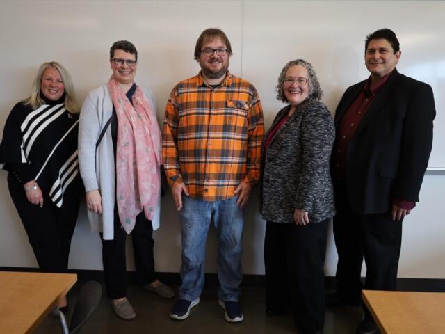 Five adults posing and smiling in a classroom in front of a whiteboard.