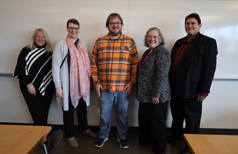 Five adults posing and smiling in a classroom in front of a whiteboard.