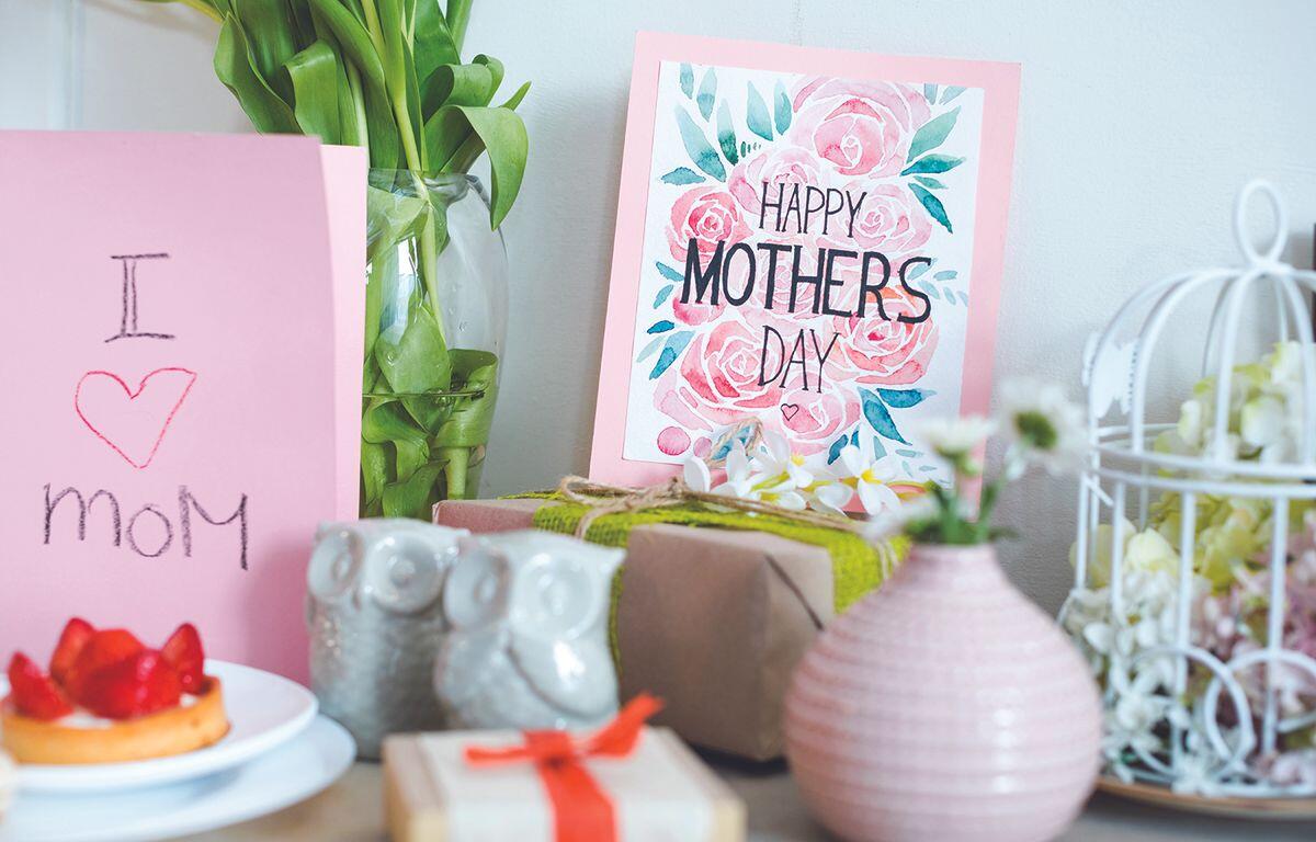 Mother's Day display with a pink 'I heart Mom' card, a floral 'Happy Mother's Day' card, wrapped gifts, and a strawberry tart on a table.