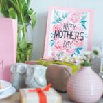 Mother's Day display with a pink 'I heart Mom' card, a floral 'Happy Mother's Day' card, wrapped gifts, and a strawberry tart on a table.