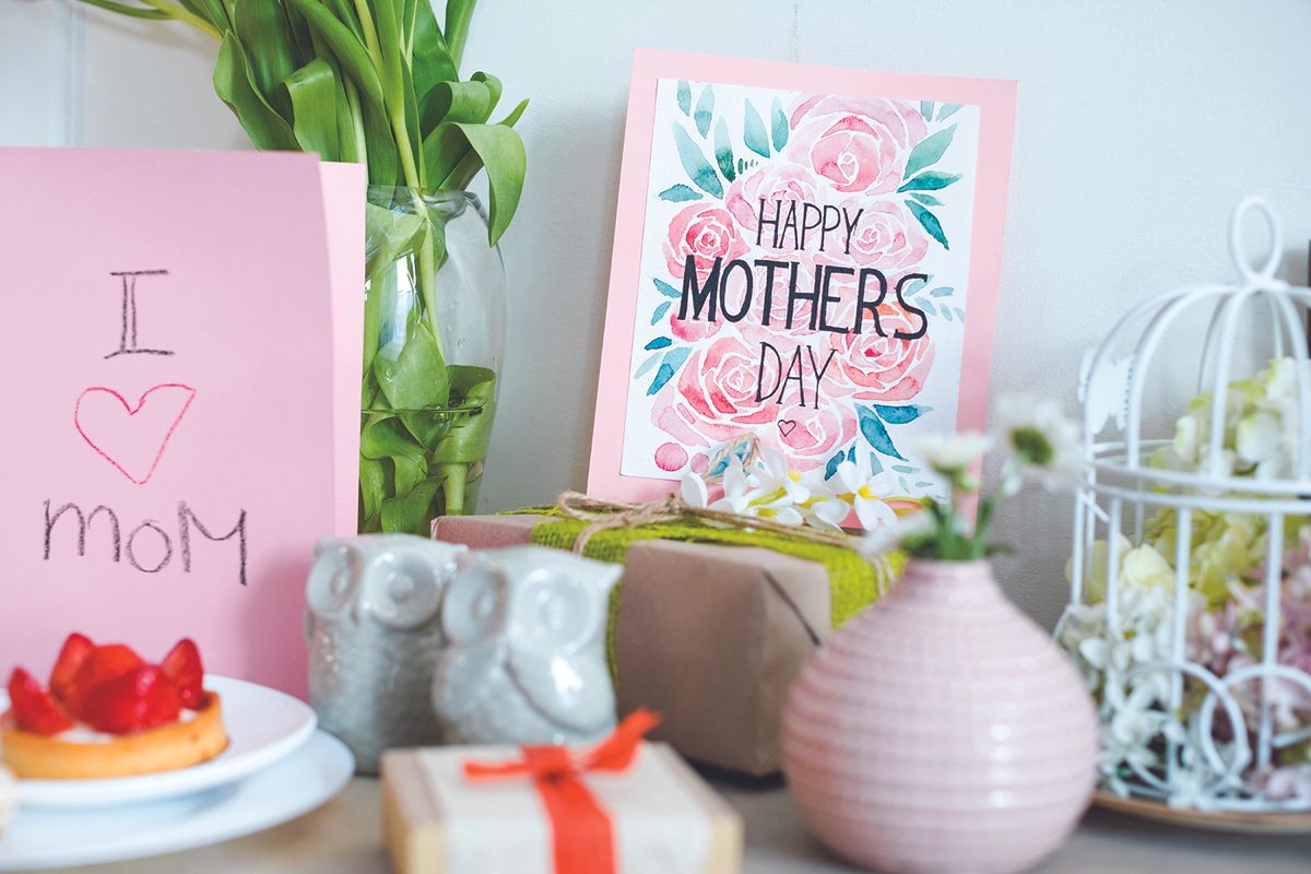 Mother's Day display with a pink 'I heart Mom' card, a floral 'Happy Mother's Day' card, wrapped gifts, and a strawberry tart on a table.