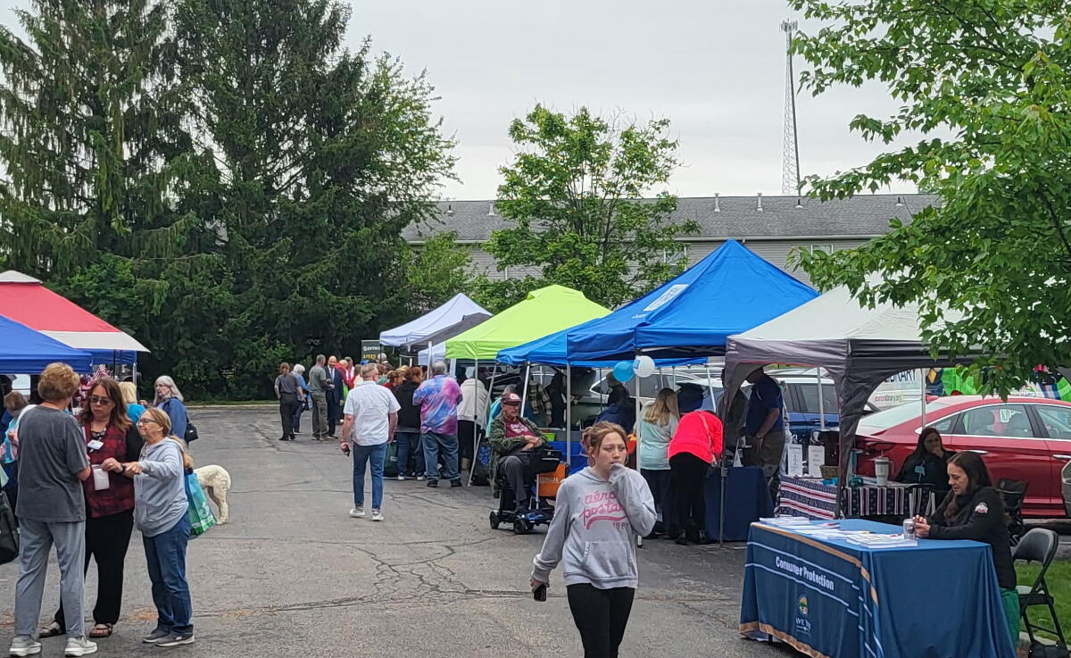 Outdoor market scene with colorful tents and people browsing stalls in a parking lot.
