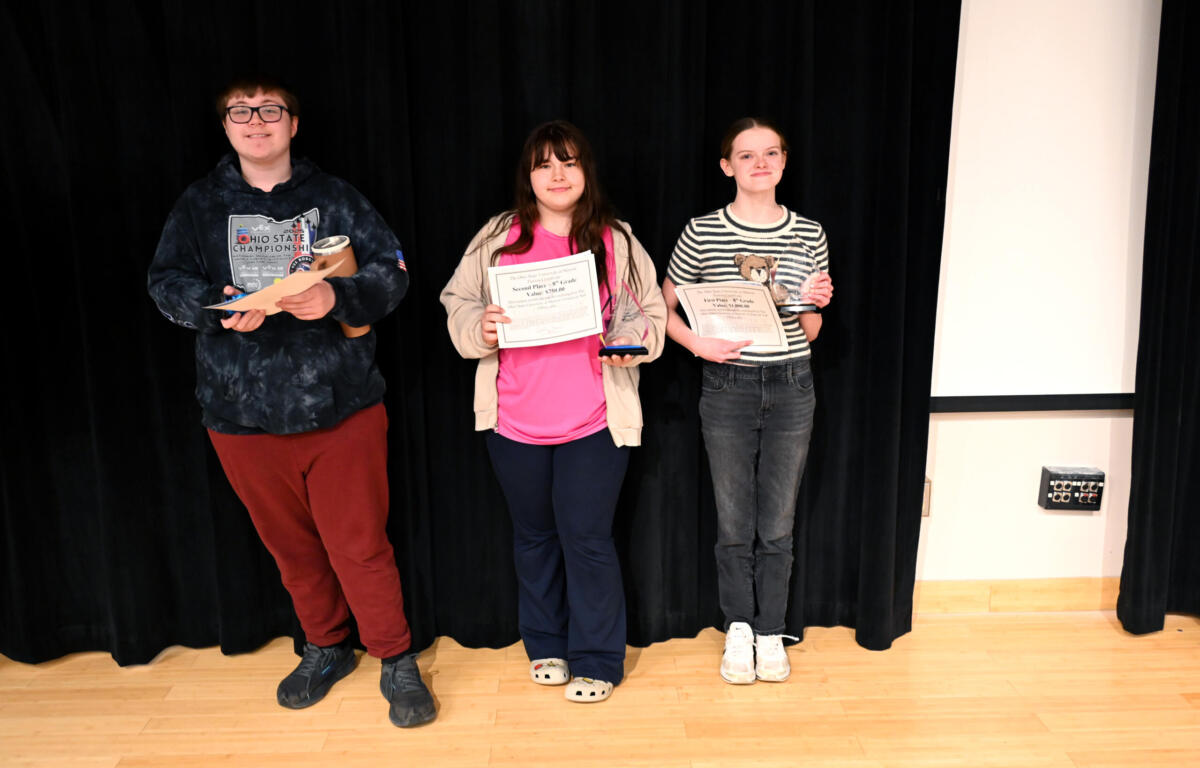 Three kids on a stage posing with awards, standing in front of a black curtain.