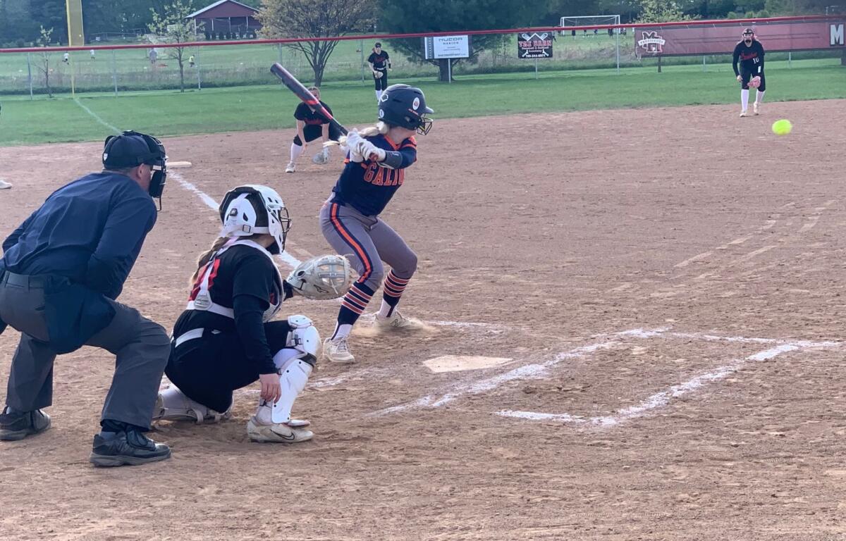Young batter in navy and orange swings at a pitch as the catcher and umpire crouch behind home plate in a youth softball game.