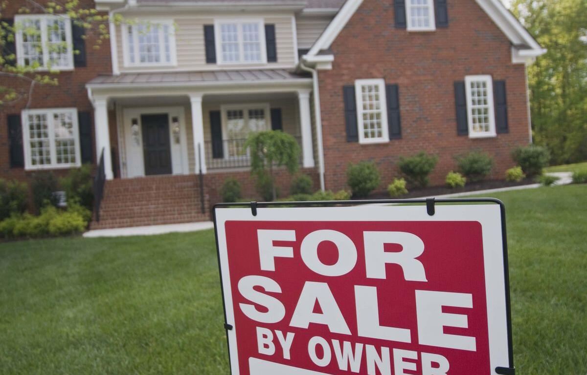 Red and white 'For Sale By Owner' sign in front yard of a brick house.