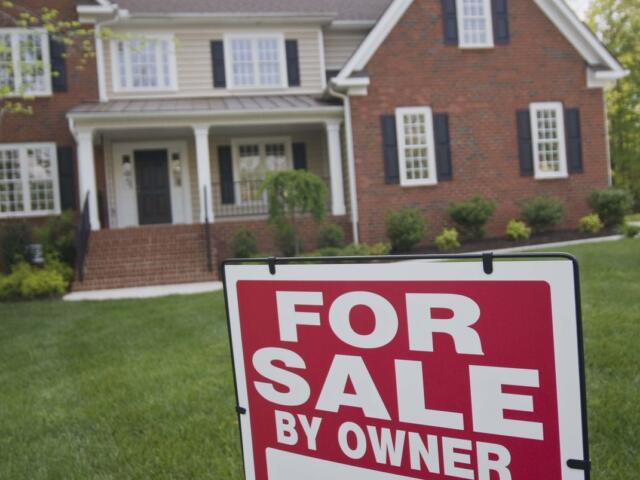 Red and white 'For Sale By Owner' sign in front yard of a brick house.