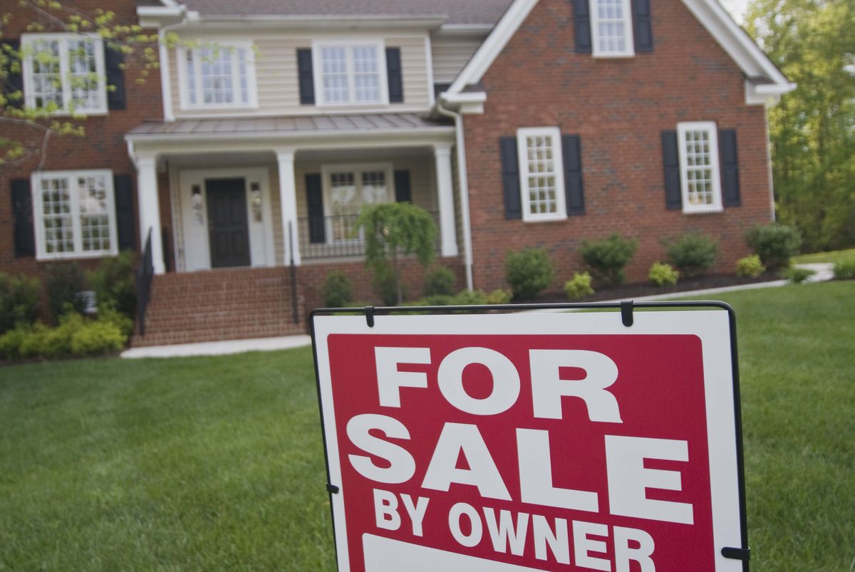 Red and white 'For Sale By Owner' sign in front yard of a brick house.