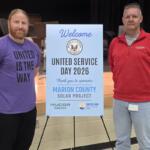 Two men stand beside a blue sign reading Welcome, United Service Day 2026, thanking sponsors for the Marion County Solar Project event on a stage backdrop.