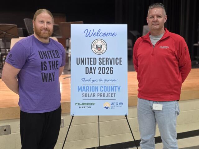 Two men stand beside a blue sign reading Welcome, United Service Day 2026, thanking sponsors for the Marion County Solar Project event on a stage backdrop.