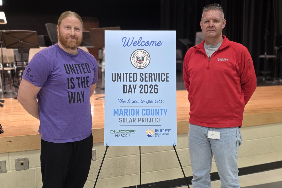 Two men stand beside a blue sign reading Welcome, United Service Day 2026, thanking sponsors for the Marion County Solar Project event on a stage backdrop.