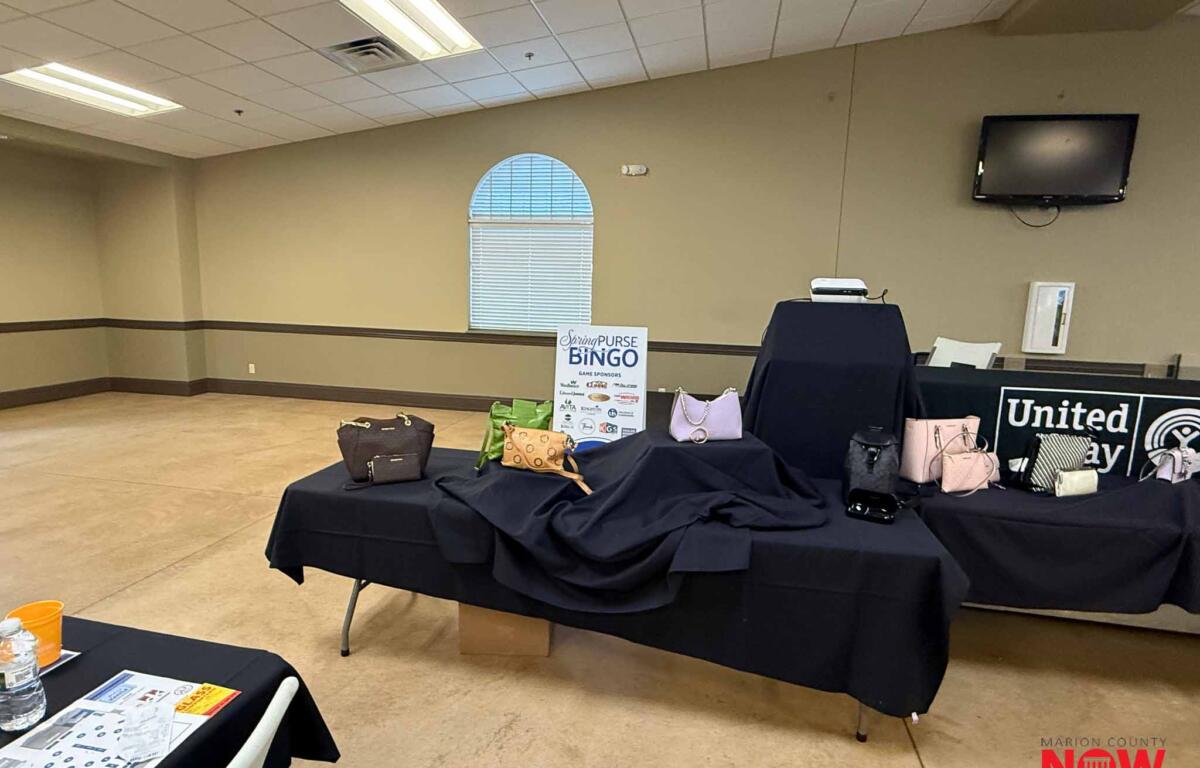 Display of handbags on black-draped tables at a fundraising event with a Spring Bingo sign in the background.