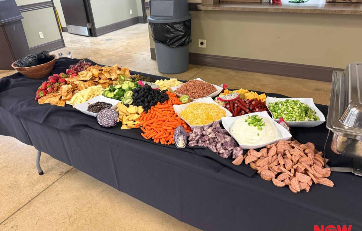 Buffet table with assortments of chips, fruits, vegetables, and dips on a black cloth, NOW logo in the corner.