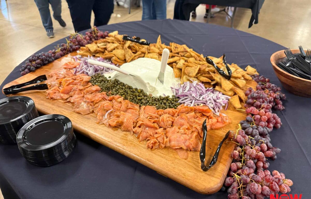 Charcuterie board with smoked salmon, cheese, crackers, grapes, red onions, and capers on a wooden board.