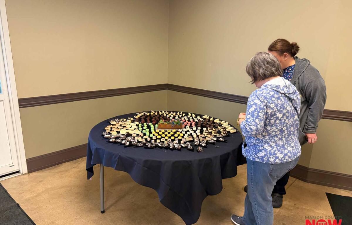 Two people stand at a round table covered with a navy cloth, examining a large display of assorted bite-sized desserts.
