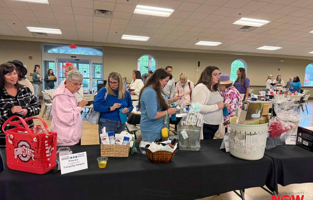 Indoor charity fundraiser with people browsing tables of prize baskets and displays in a large room.