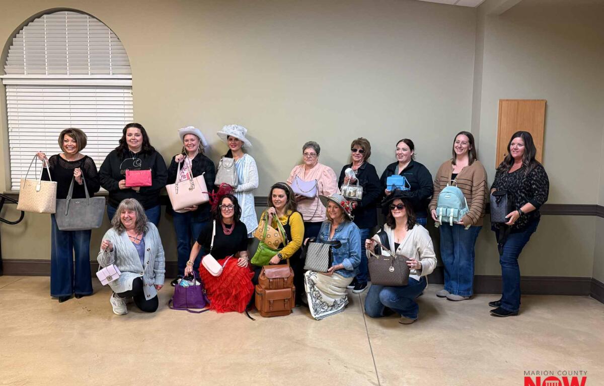Group of women posing with assorted handbags indoors, some kneeling in front; Marion County NOW logo bottom right.