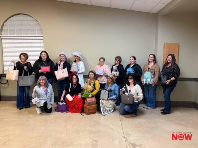 Group of women posing with assorted handbags indoors, some kneeling in front; Marion County NOW logo bottom right.