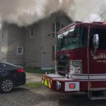 Fire engine from Marion Fire Department in front of a gray two-story house with thick smoke venting from the roof.