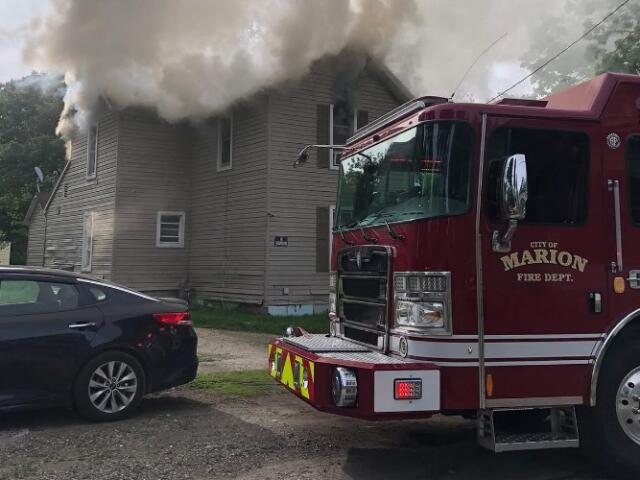 Fire engine from Marion Fire Department in front of a gray two-story house with thick smoke venting from the roof.