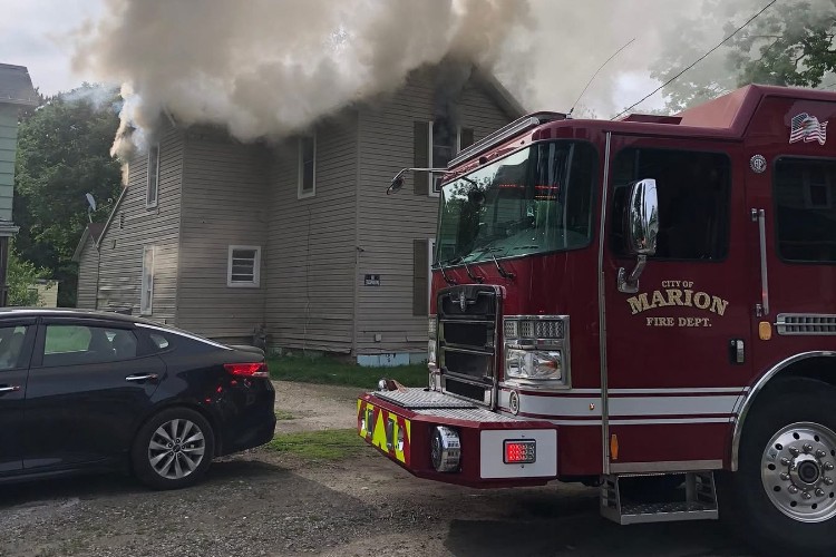 Fire engine from Marion Fire Department in front of a gray two-story house with thick smoke venting from the roof.