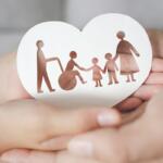 Heart-shaped card with brown cutout of a family: a person in a wheelchair, two children, and two adults holding hands, cradled in protective hands.