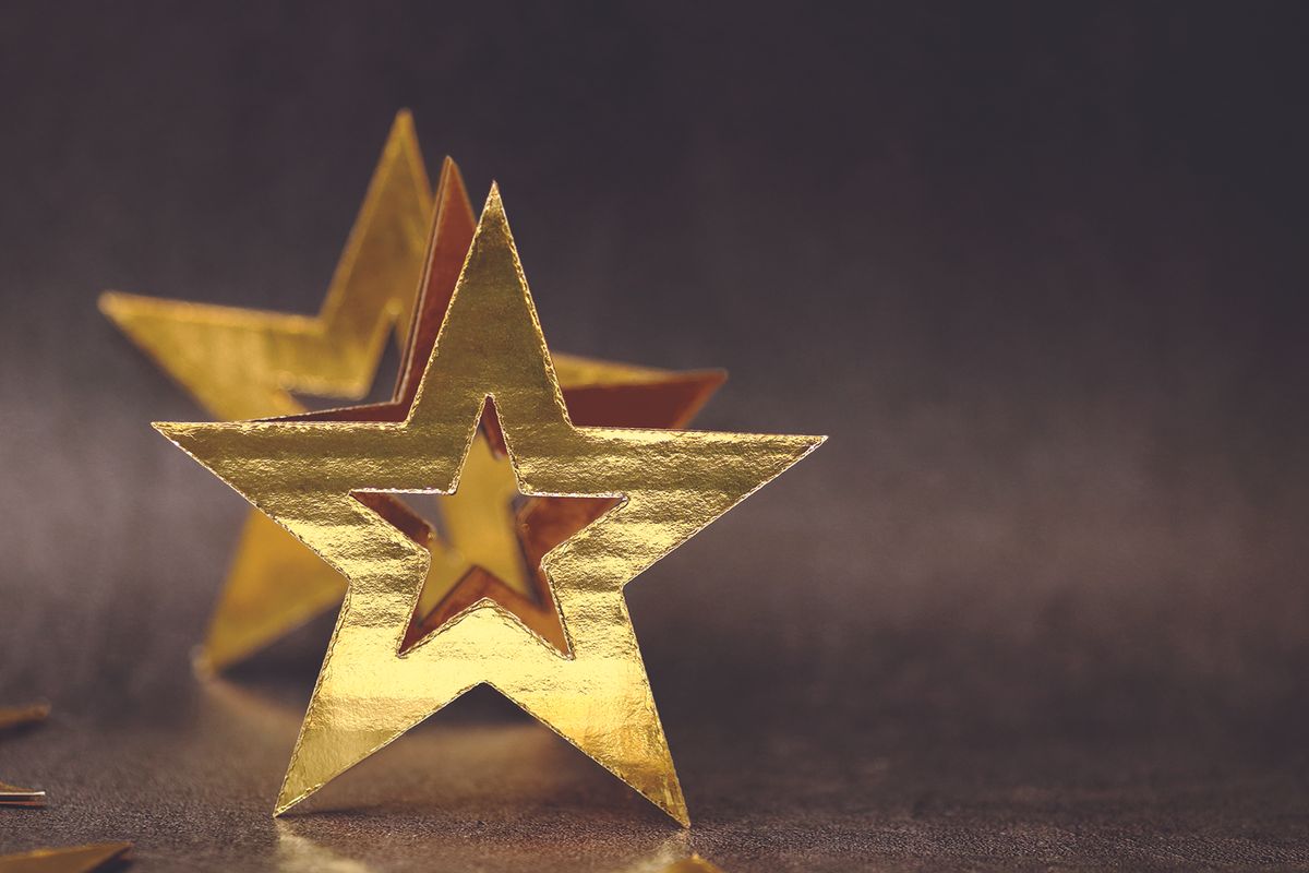 Gold foil star decorations on a dark, shallowly blurred background, with one star in front and another behind.