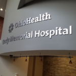 Curved wall inside a hospital lobby with large illuminated sign reading 'OhioHealth Grady Memorial Hospital'.