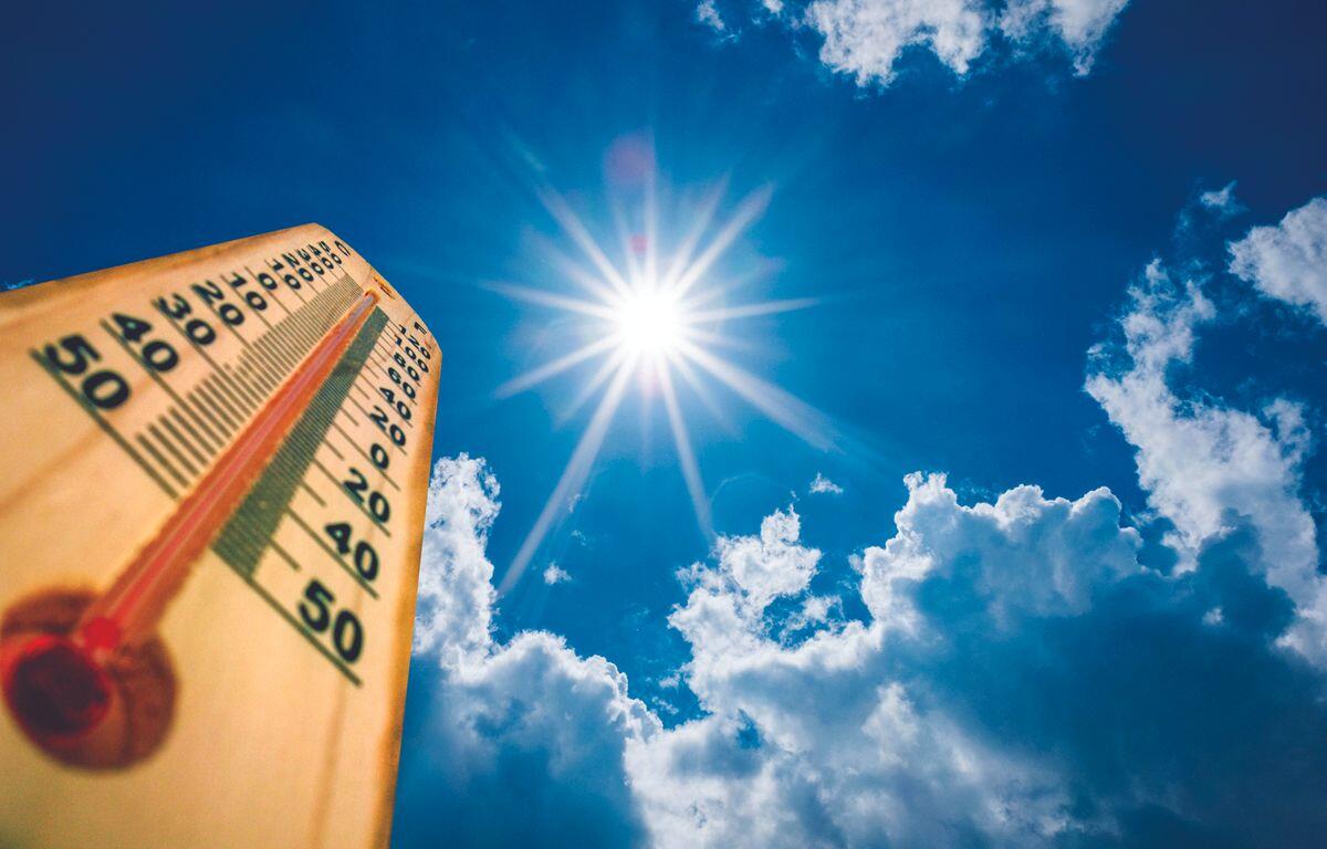 Wooden thermometer angled toward a bright sun in a clear blue sky with fluffy clouds, indicating hot weather
