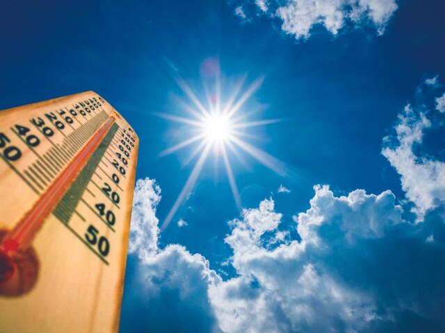 Wooden thermometer angled toward a bright sun in a clear blue sky with fluffy clouds, indicating hot weather