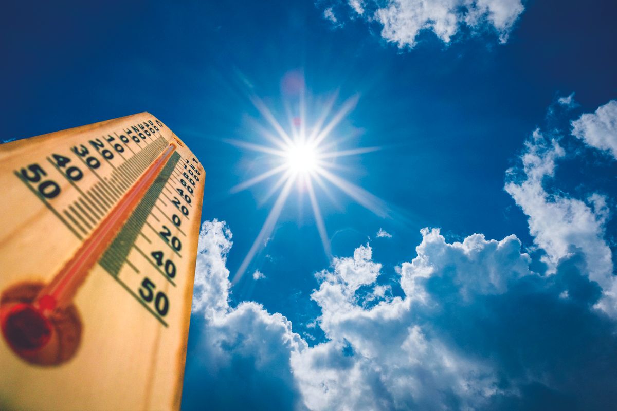 Wooden thermometer angled toward a bright sun in a clear blue sky with fluffy clouds, indicating hot weather