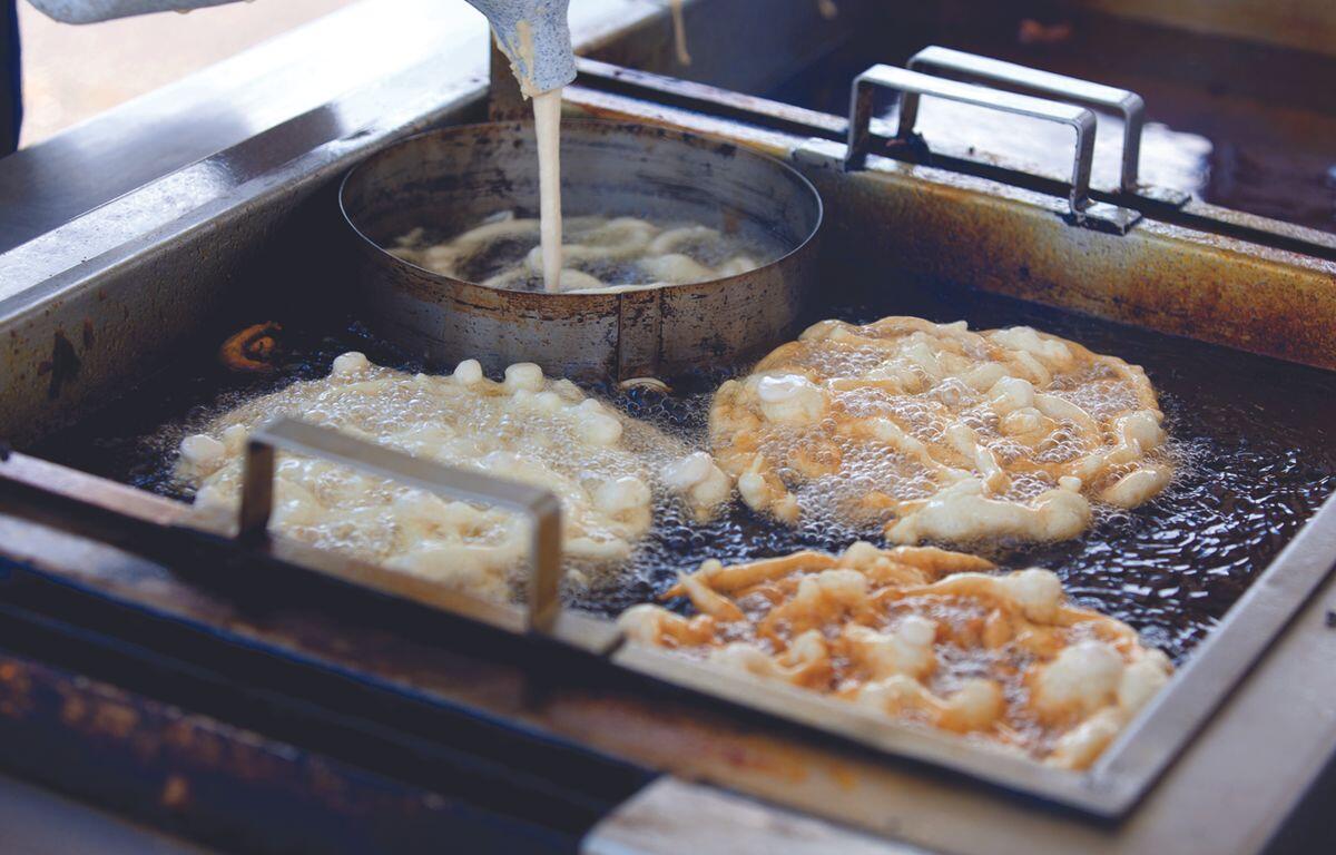 Frying station with dough pieces bubbling in hot oil in a commercial deep fryer.