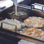 Frying station with dough pieces bubbling in hot oil in a commercial deep fryer.
