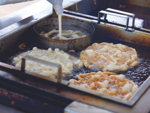 Frying station with dough pieces bubbling in hot oil in a commercial deep fryer.