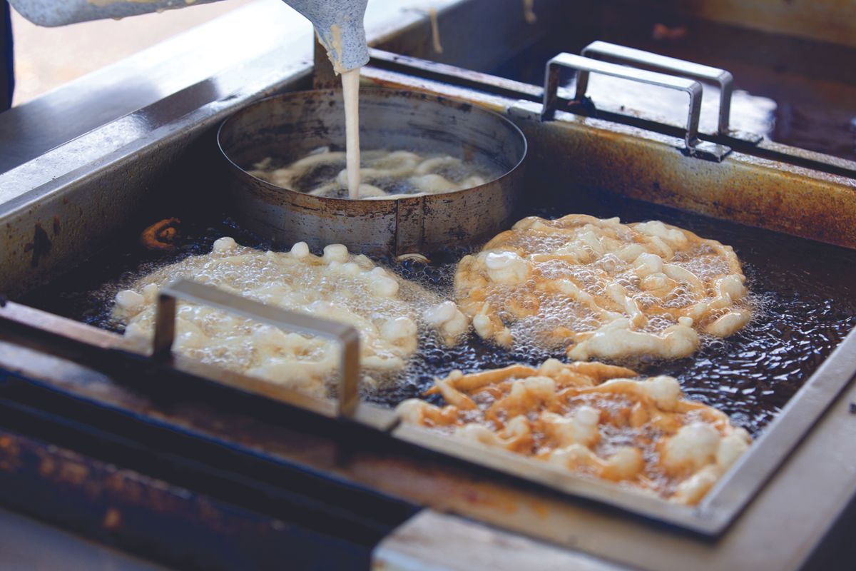 Frying station with dough pieces bubbling in hot oil in a commercial deep fryer.