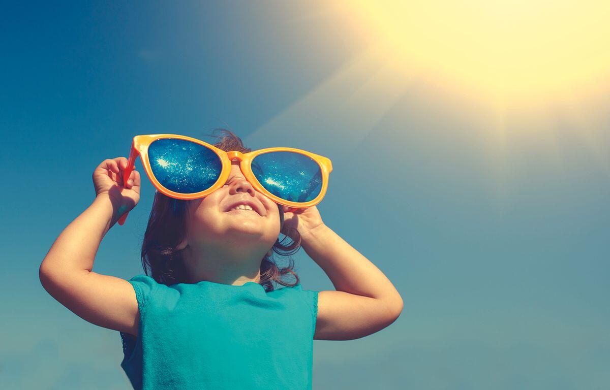 Young girl wearing bright orange oversized sunglasses, looking up at the sunny sky.