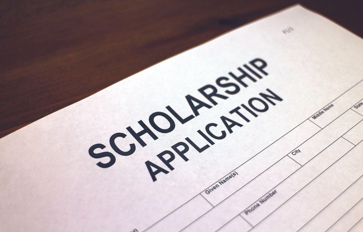 Close-up of a white scholarship application form on a wooden desk, with bold title SCHOLARSHIP APPLICATION visible.