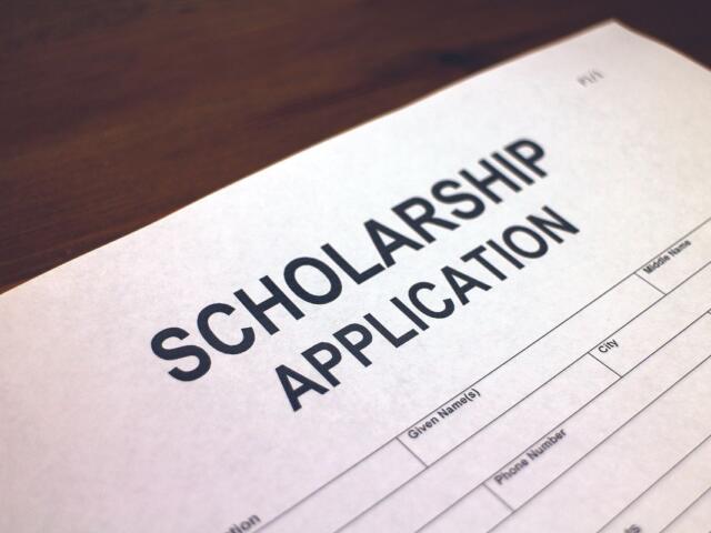 Close-up of a white scholarship application form on a wooden desk, with bold title SCHOLARSHIP APPLICATION visible.