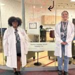 Two students in white lab coats stand outside a glass-walled Buckeye Language Network Language Pod; OSU signage visible inside.