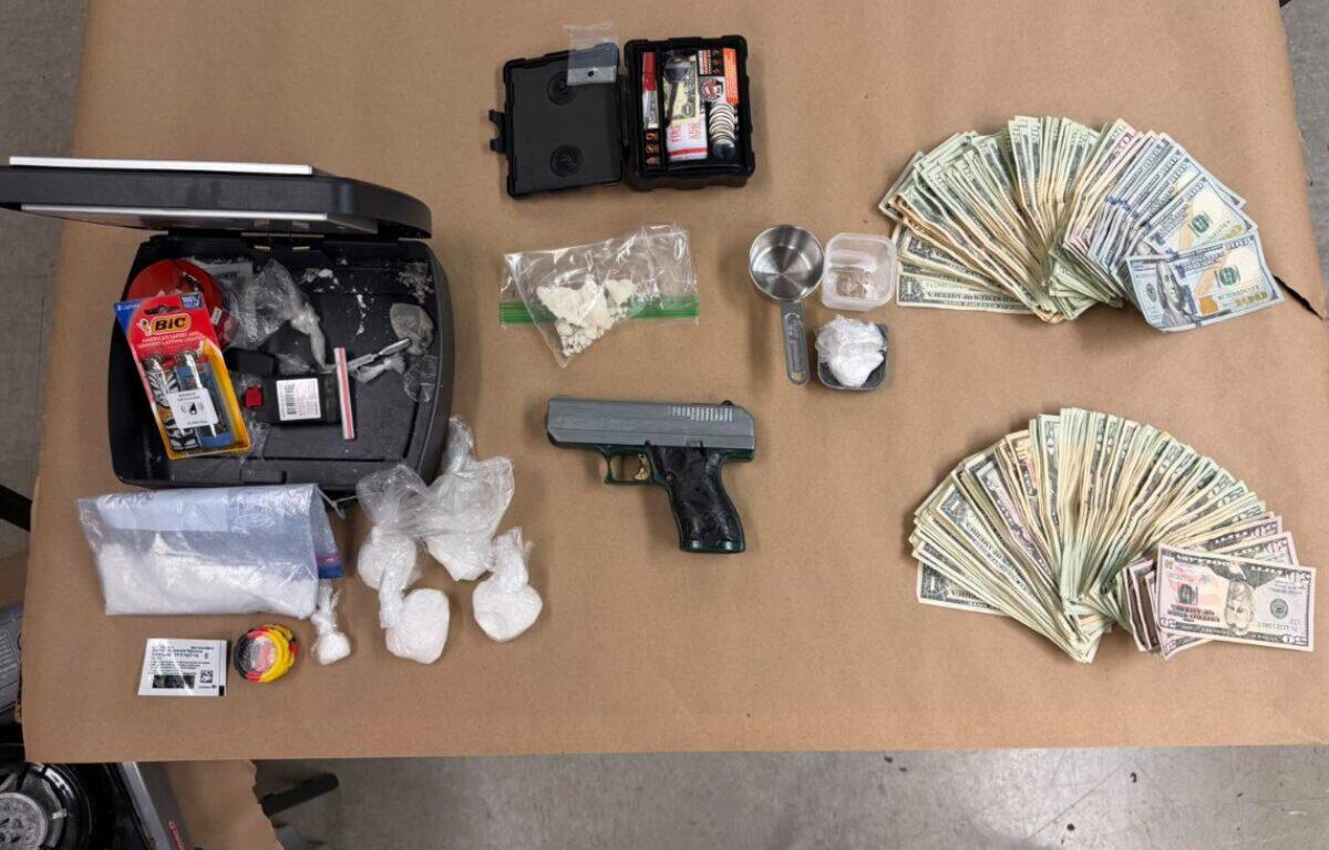 Top-down view of a handgun, plastic bags of white powder, a scale, and large stacks of cash laid out on a table, suggesting drug dealing paraphernalia.