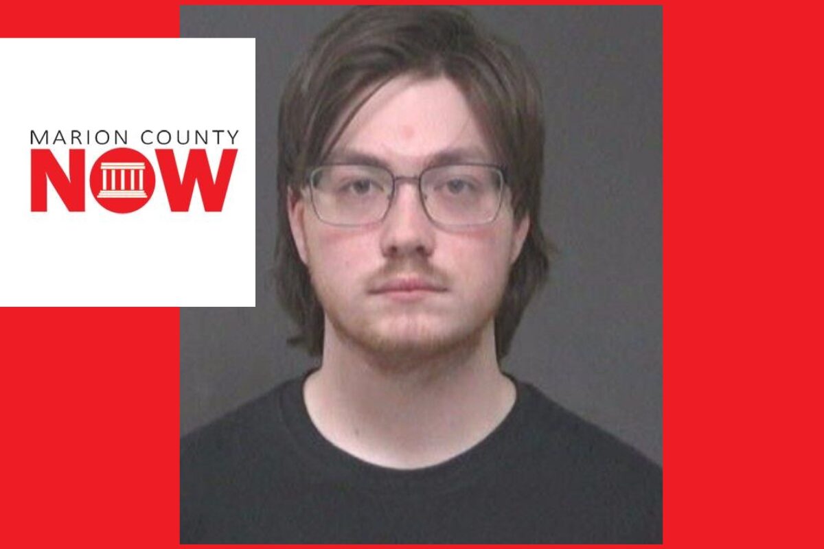Mugshot-style photo of a young man with glasses and dark hair wearing a black shirt, against a gray backdrop, with a Marion County NOW logo overlay on the left and a red background.