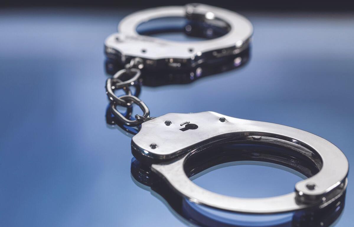 Metal handcuffs connected by a short chain on a reflective blue surface, close-up shot.