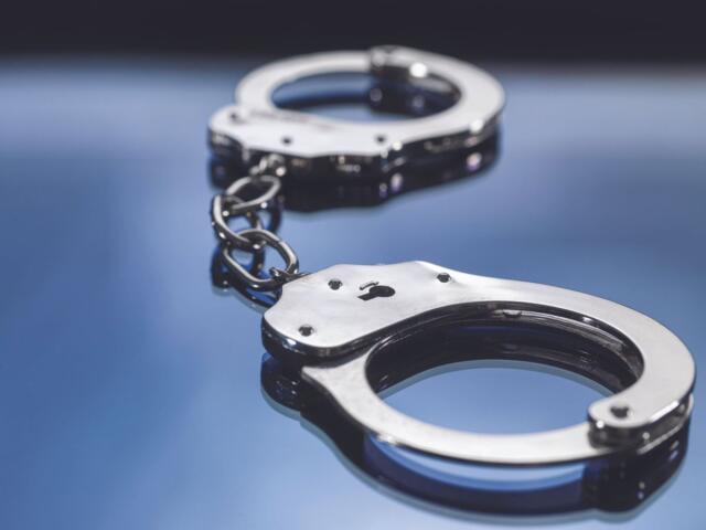 Metal handcuffs connected by a short chain on a reflective blue surface, close-up shot.
