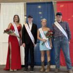 Four pageant contestants stand on a stage in front of red, white, and blue curtains, wearing sashes and crowns, and holding bouquets.